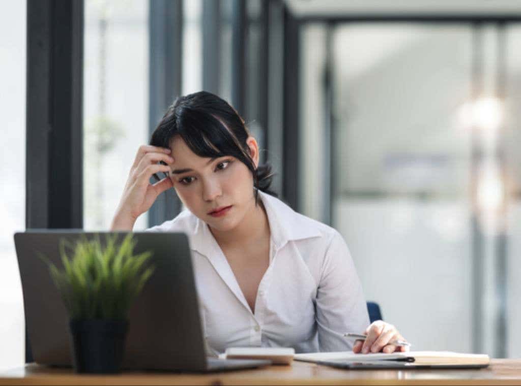 Stressed business woman working at office on laptop and document, looking worried, tired and overwhelmed.