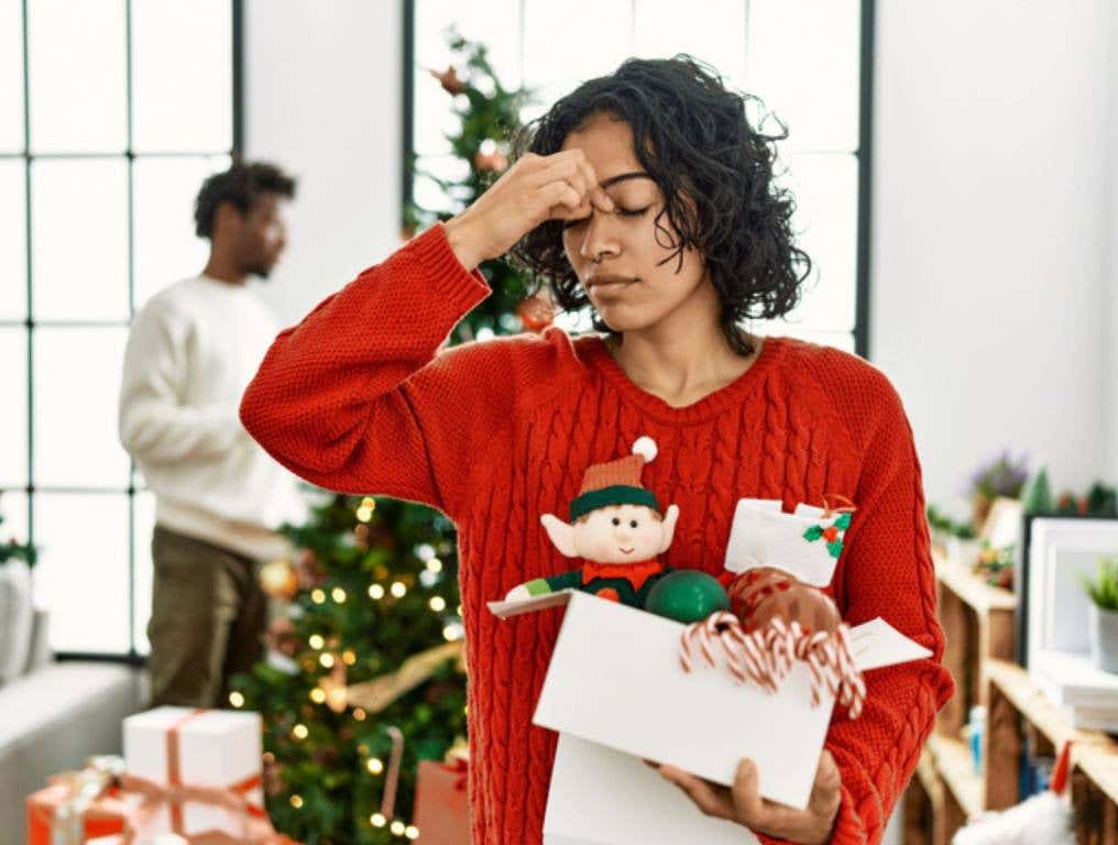 woman standing by christmas tree with decoration tired rubbing nose and eyes feeling fatigue and headache., holiday stressors and headache concept