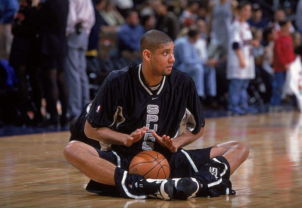 Tim Duncan sitting on the court with a basketball on his lap