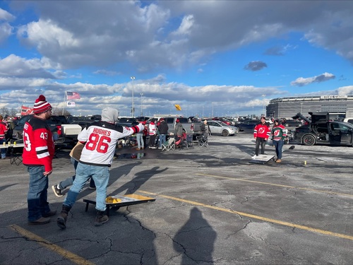 men in New Jersey devils jerseys playing corn hole in the parking lot